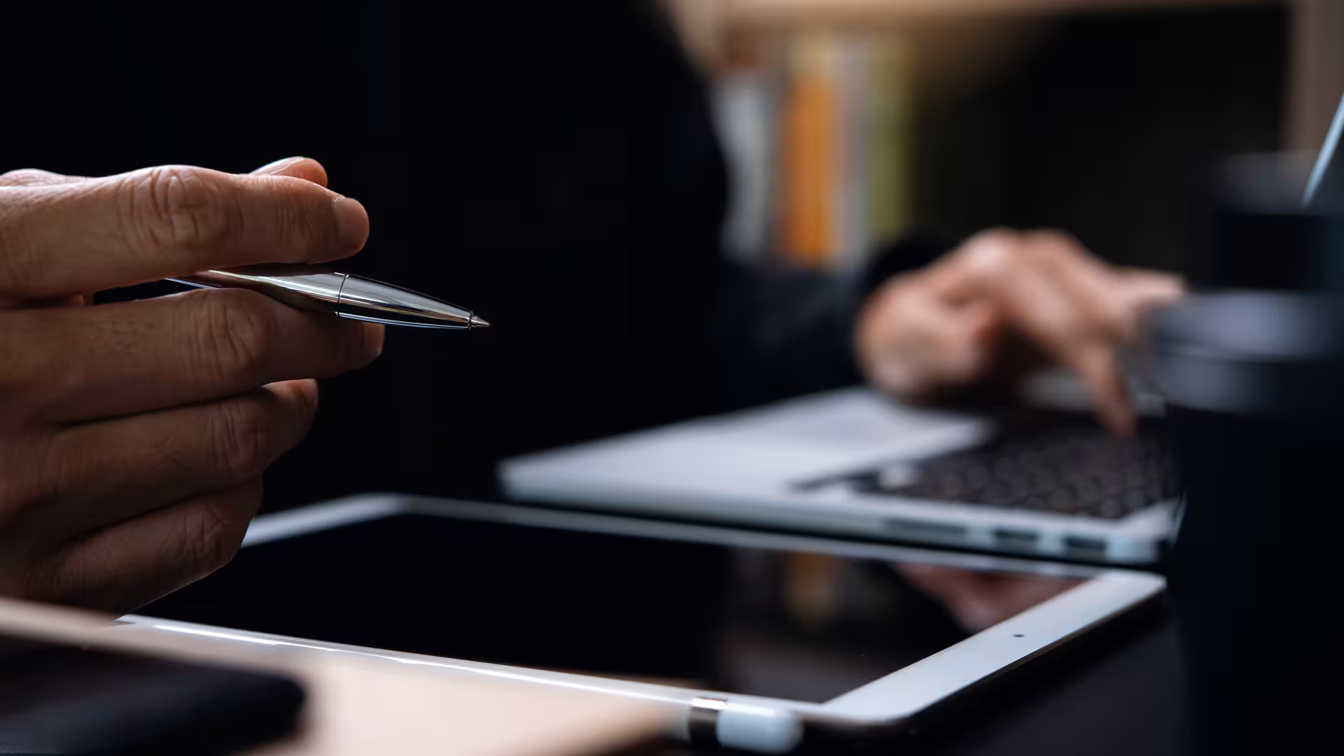 Person sitzt am Schreibtisch mit Tablet und Stift in der Hand