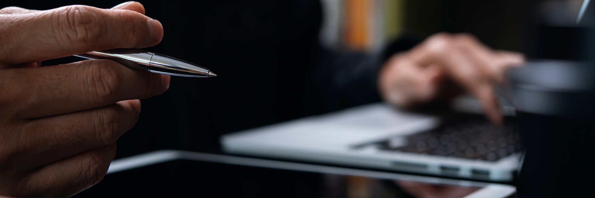 Person sitzt am Schreibtisch mit Tablet und Stift in der Hand